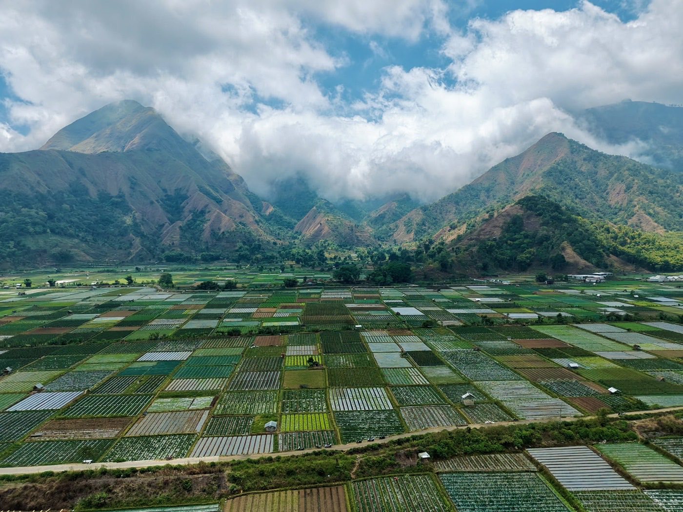 Cloud pouring over the volcanic ridges above the Sembalun valley, vegetable fields stretching out below.