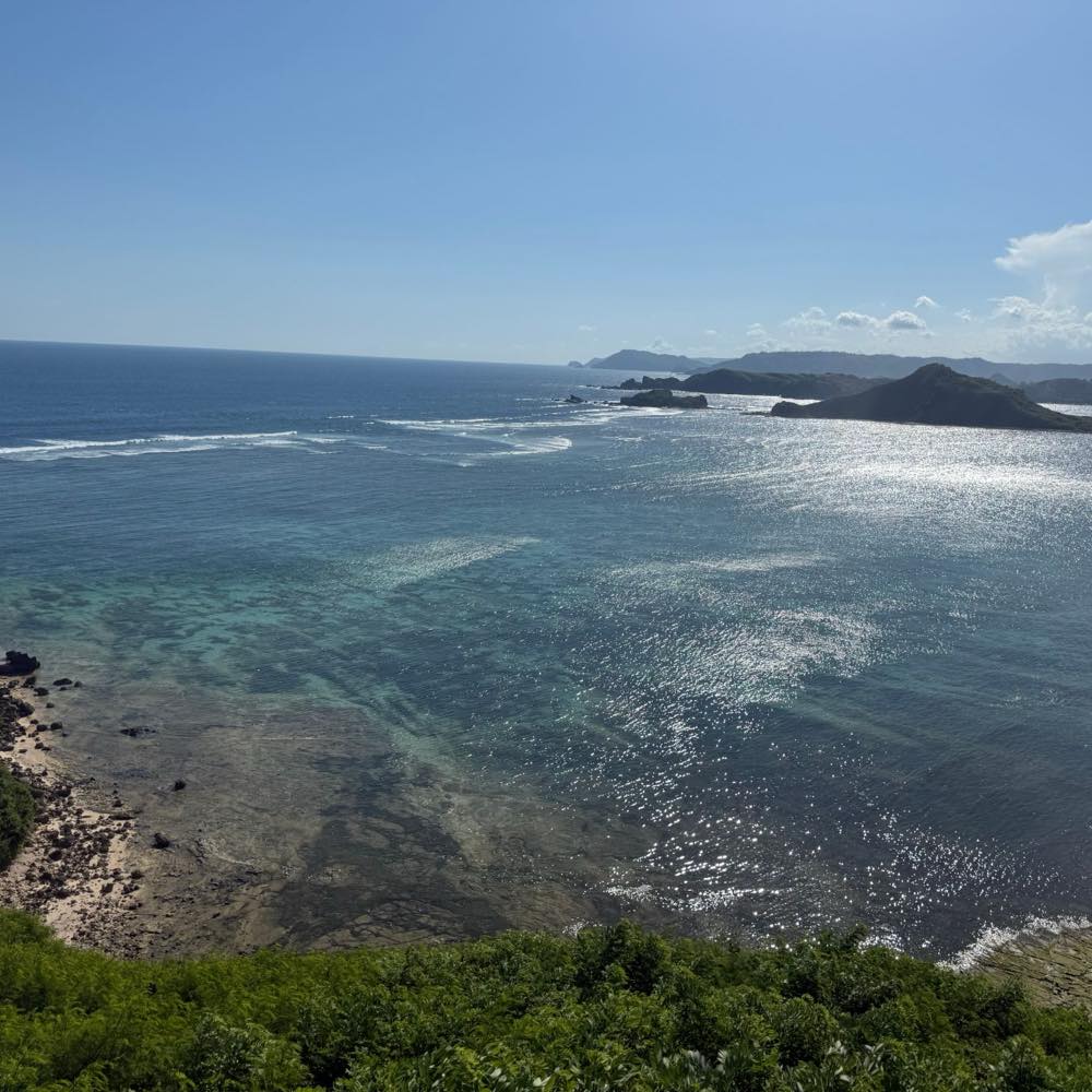A bay on the south coast of Lombok seen from a headland, reef visible through clear water and green hills beyond.